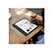 Person schreibt mit Stift auf einem Tablet, das auf einem Holztisch liegt. Im Hintergrund ist ein Kaffeegedeck.