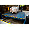 A worker in work clothes stands next to a loading ramp on which a package stands on a pallet.