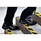 Person stepping up stairs, black shoes, yellow and black warning stripes on steps.