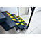 Steel staircase with yellow and black warning stripes. Handrail on the right, door and tiles in the background.