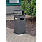 Grey outdoor trash bin with shelf, rectangular with cutouts. Standing on paving stones next to green areas.