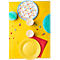 Table jaune avec décorations de fête : assiettes, gobelets, serviettes, confettis et guirlandes.