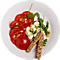 Salade de tomates et mozzarella sur une assiette blanche, avec des gressins.