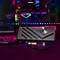 Schwarze AVerMedia PCIe-Capture-Karte vor einem Gaming-PC mit pinker Beleuchtung.
