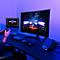 Ein Gamer spielt mit einem Controller vor einem großen Monitor, auf dem ein Rennspiel in blauem Umgebungslicht läuft.