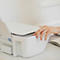 Main actionnant une imprimante blanche moderne sur un bureau lumineux.