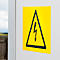 Yellow warning sign with black lightning bolt in a triangle on a white wall.