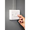 A finger presses a light switch on. The switch is fixed in a white holder on a gray wall.