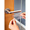 Hands holding a transparent protective film to cover a metal door handle. The door handle is attached to a wooden door.