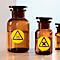 Two brown glass bottles with black lids and yellow warning signs. One shows a skull, the other a cross. Liquid is visible.