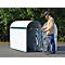 Man putting a bicycle into a white bicycle garage. He wears a helmet and a jacket.