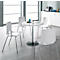 Four white chairs surround a round table. The table has a silver column and a black base. Light wooden parquet.