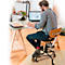 Ein Mann mit Brille sitzt an einem Tisch, er arbeitet am Laptop und schreibt. Er trägt ein kariertes Hemd, Jeans, rote Socken.