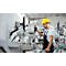 Un homme portant un casque jaune travaille sur une machine dans une usine. Il porte une salopette et un t-shirt blanc.