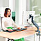 Une femme souriante est assise à un bureau et travaille sur un ordinateur. Elle porte un haut blanc et une jupe verte.