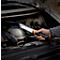 Une personne tient une lampe LED dans le compartiment moteur d'une voiture. La lampe est allumée. Le compartiment moteur est ouvert.