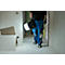 Persoon draagt lamp door gang in ruwbouw, blauwe werkkleding.