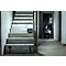 Un homme s'agenouille sur un chantier et tient une lampe de travail brillante. Escalier et lampe à droite, gros œuvre à gauche.