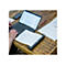 Person arbeitet an einem Laptop. Ein Blatt Papier liegt in einem Scanner. Auf dem Holztisch sind auch Smartphone und Stift.