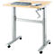 Bureau réglable en hauteur avec ordinateur portable et bloc-notes. Plateau de table brun clair, cadre argenté, roulettes noires. Manivelle pour le réglage en hauteur.