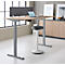 Bureau clair avec cadre réglable en hauteur, ordinateur portable et tabouret; mur gris en arrière-plan.