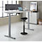 Un bureau réglable en hauteur avec un ordinateur portable, une chaise, un mur rembourré gris et des accessoires. Aménagement de bureau lumineux et moderne.