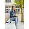 Jeune femme assise sur un mur, écrivant dans un carnet et souriant. Elle porte un jean, une veste en jean et des baskets.