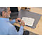 Un homme écrit dans un cahier sur un bureau. Un tapis de bureau gris et un ordinateur portable sont sur la table.