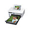 Ein weißer Canon SELPHY CP1000 Fotodrucker druckt ein Foto eines lächelnden Mädchens. Das Foto wird aus dem Drucker geschoben und ist auch im Display zu sehen.