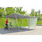 Person with a bicycle under a metal bike shelter. A green wall is behind the person. Trees in the background.