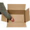 A person's hand reaching into an open brown cardboard box. The box walls are made of corrugated cardboard.