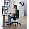 Une jeune femme est assise à un bureau et travaille sur l'ordinateur. Elle porte des lunettes et un jean.