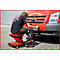 Un homme est assis sur un tabouret roulant rouge devant un fourgon Ford rouge et travaille.