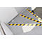Staircase with yellow and black warning stripes, grey floor, light wall. The warning stripes mark the edges of the stairs.