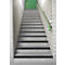 Stairs with gray steps, black stripes and a green handrail. At the end of the stairs is a green door.