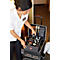 A hotel employee opens a service cart. Bottles, utensils, and cleaning supplies are in the cart. She wears a white blouse and black pants.