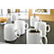 White coffee cups on a table. One cup with coffee, one with a spoon, nuts in a glass bowl.