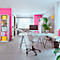 Modernes, helles Büro mit rosa Akzentwänden, Schreibtisch, Bürostuhl und Pflanzen. Im Hintergrund ist ein Sofa zu sehen.
