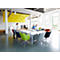 A conference room with people. A woman stands at the table, others are sitting and working. Colorful chairs.