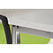 Close-up: White table top with metal legs and green background, part of a chair visible.