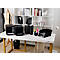 Bureau de bureau avec plateaux noirs, porte-lettres, porte-stylo, lampe, buste de couturière, livres et orchidées.