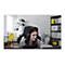 Eine lächelnde Frau mit Headset sitzt vor einem Computer. Im Hintergrund: Regal, gelber Stuhl, Sofa.