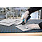 Une personne portant des gants de travail découpe un morceau de feutre gris avec un couteau Martor sur un tapis de découpe.