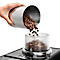 Hand hält metallenen Behälter, aus dem Kaffeebohnen in einen durchsichtigen Behälter fließen. Teil einer Kaffeemaschine.