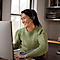 Smiling woman with a headset in front of a PC. She is sitting at a desk with a window in the background.