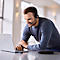 A man wearing a headset, smiling and looking at a laptop.