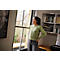 Woman with headset looks out of a window in an office. She smiles relaxed, arm on hip.