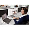 A man wearing a headset at a desk, in a video call, a woman can be seen on the monitor, other people in the background.