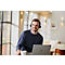 A man wearing a headset smiles while working on a laptop, holding a mug.