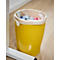 Yellow trash can with paper bag filled with waste, stands on parquet floor.